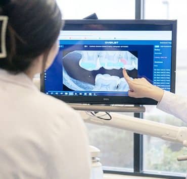 dental professionals using digital dentistry tools to examine and explain imaging results to a patient