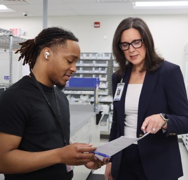 two individuals discussing papers in what appears to be a medical or clinical supply setting