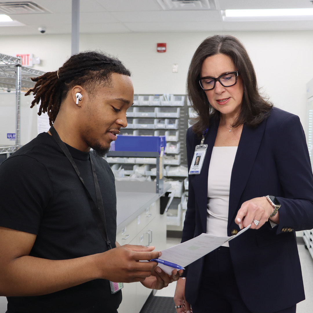 two individuals discussing papers in what appears to be a medical or clinical supply setting