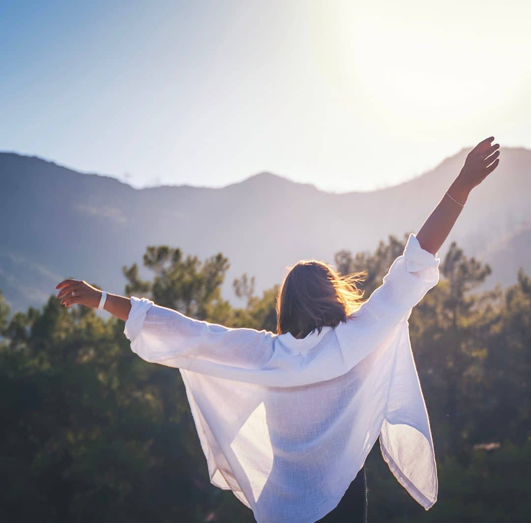 a woman from behind with her arms stretched wide against a scenic mountain backdrop