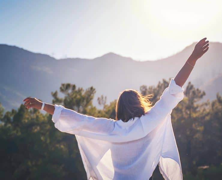 a woman from behind with her arms stretched wide against a scenic mountain backdrop
