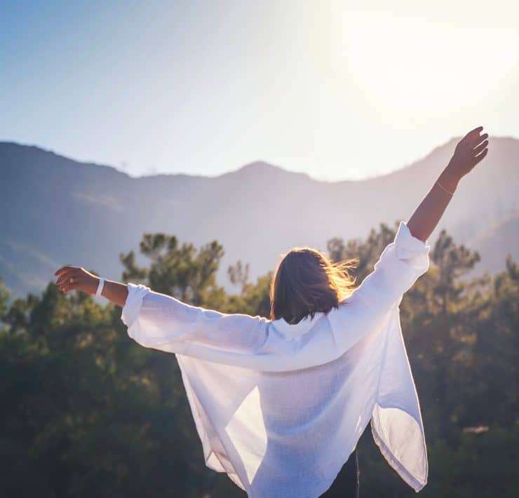 a woman from behind with her arms stretched wide against a scenic mountain backdrop