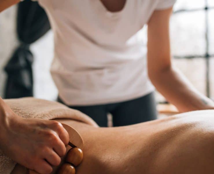 Physical therapist using a wooden massage tool during soft tissue treatment on a patient’s back.