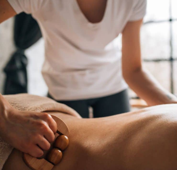 Physical therapist using a wooden massage tool during soft tissue treatment on a patient’s back.