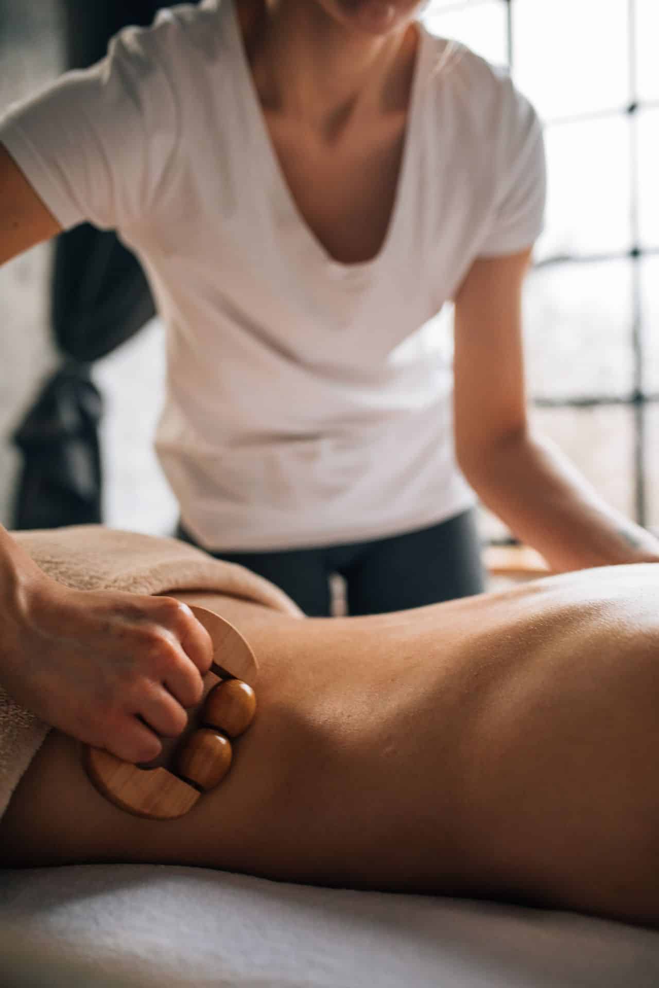 Physical therapist using a wooden massage tool during soft tissue treatment on a patient’s back.