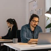 Two virtual assistants wearing headsets work on laptops in a modern office, providing remote administrative support.