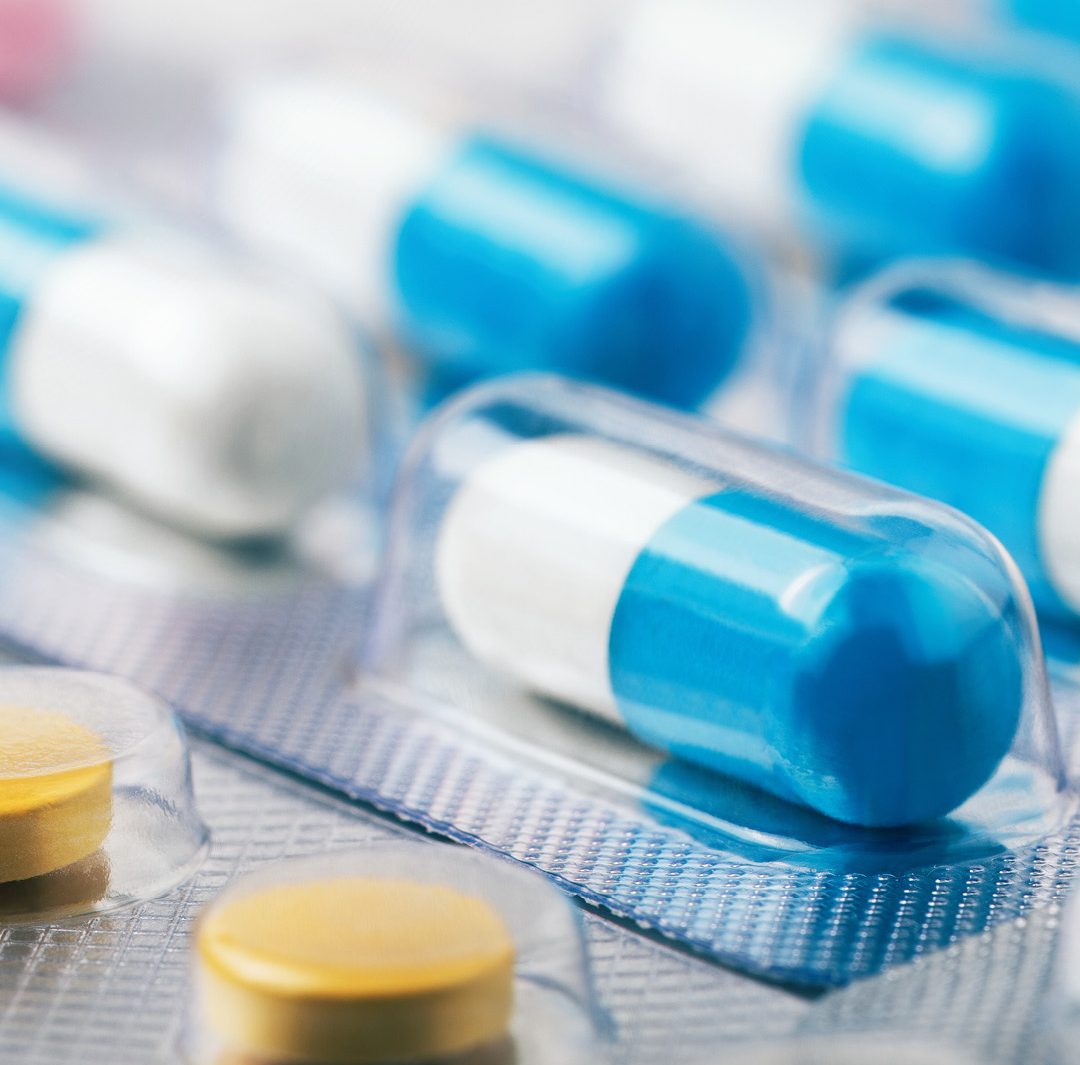 several blue-and-white hard gel capsules packed in clear blister packs, alongside round yellow tablets