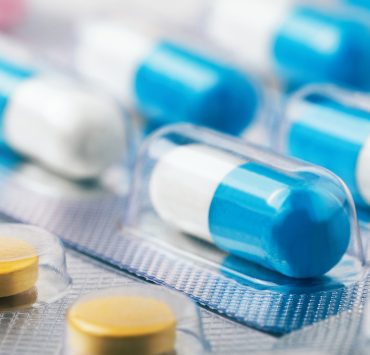several blue-and-white hard gel capsules packed in clear blister packs, alongside round yellow tablets