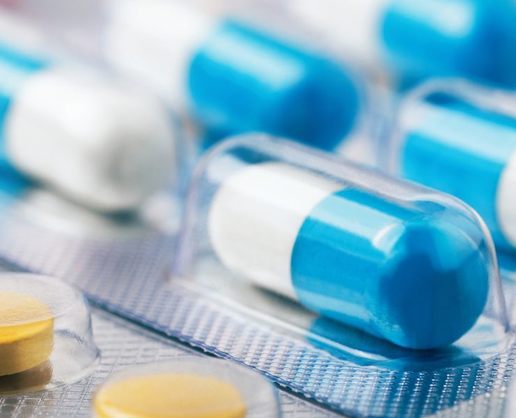 several blue-and-white hard gel capsules packed in clear blister packs, alongside round yellow tablets