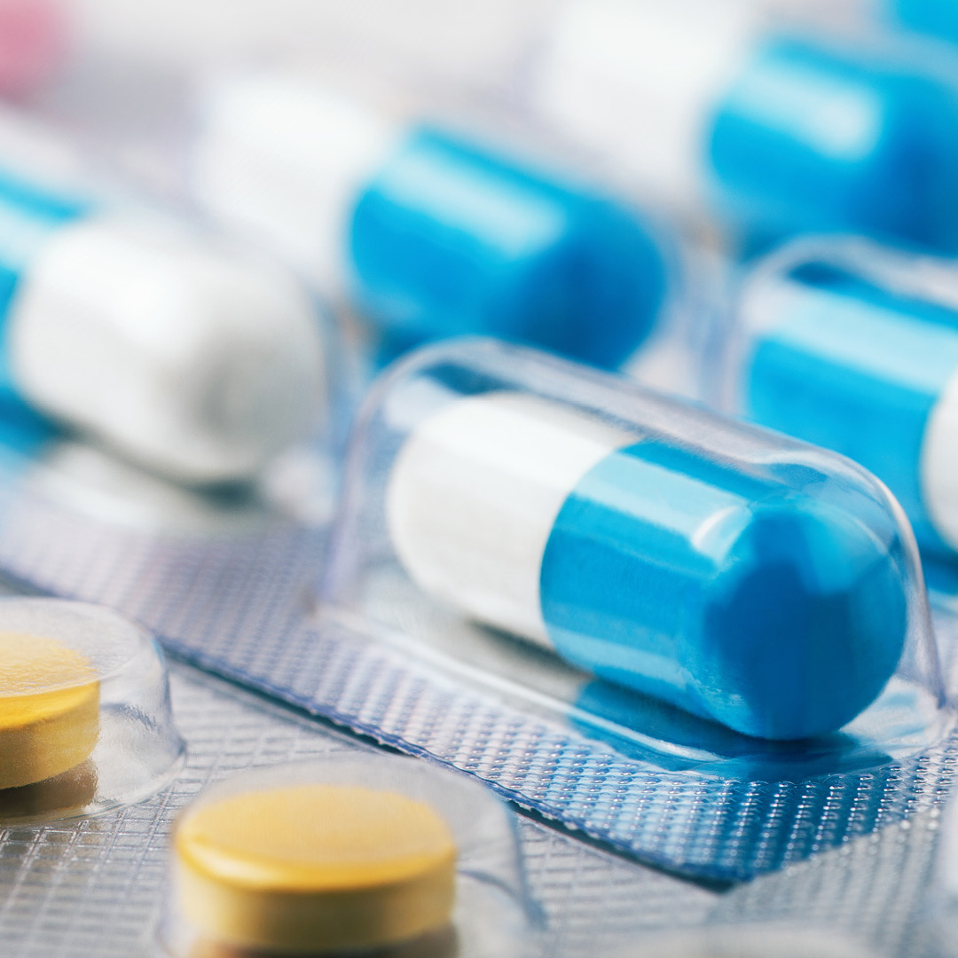 several blue-and-white hard gel capsules packed in clear blister packs, alongside round yellow tablets