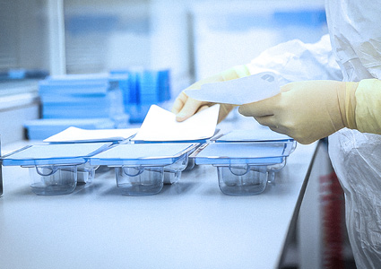 a person wearing a lab coat and gloves working in a cleanroom or laboratory environment, handling sterile medical or pharmaceutical packaging and components