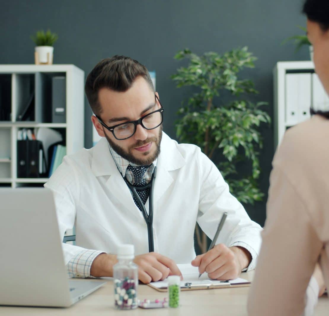 Doctor writing notes during a consultation with a patient in a medical office.
