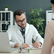Doctor writing notes during a consultation with a patient in a medical office.