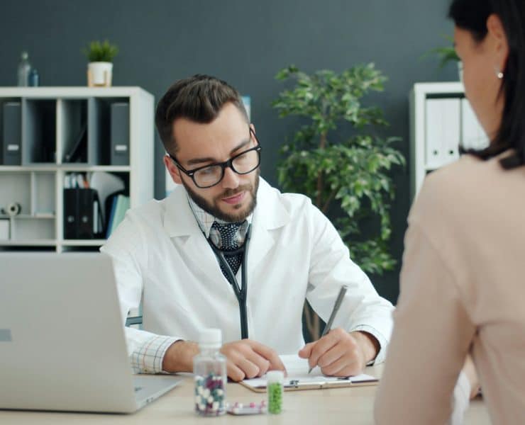 Doctor writing notes during a consultation with a patient in a medical office.