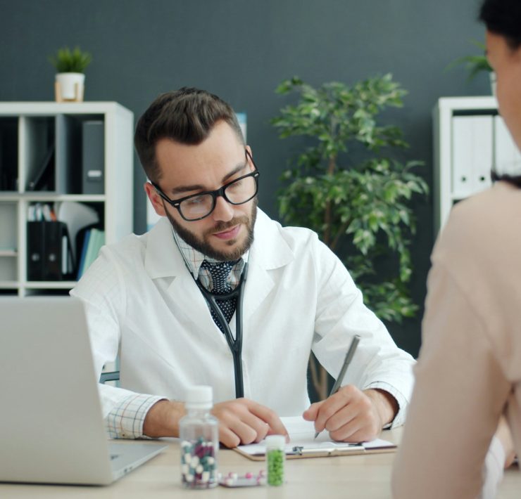 Doctor writing notes during a consultation with a patient in a medical office.