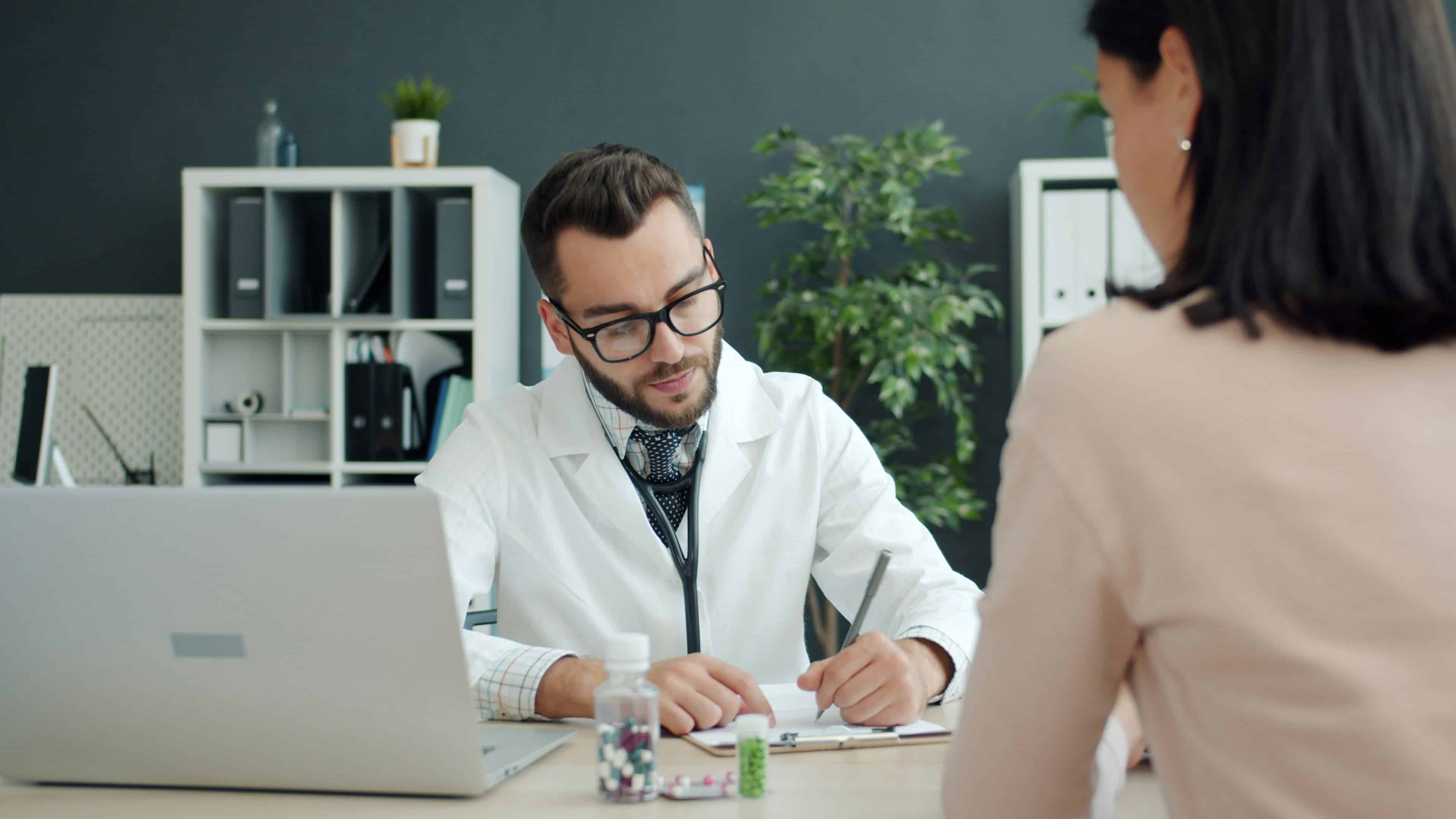 Doctor writing notes during a consultation with a patient in a medical office.