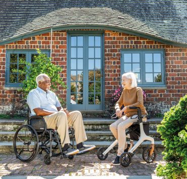 a man sitting in a wheelchair and a woman seated on a rollator walker outside a brick building