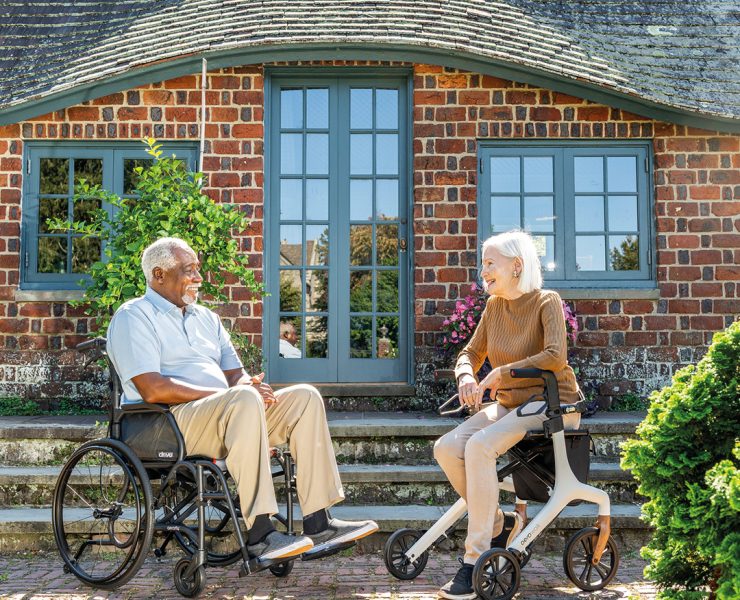 a man sitting in a wheelchair and a woman seated on a rollator walker outside a brick building