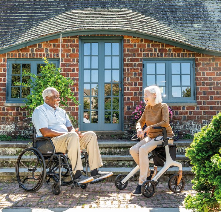 a man sitting in a wheelchair and a woman seated on a rollator walker outside a brick building