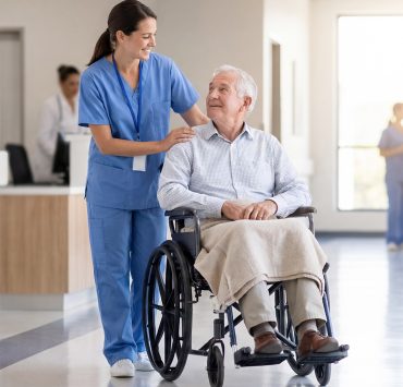 a healthcare worker in blue scrubs assisting a senior male patient seated in a wheelchair