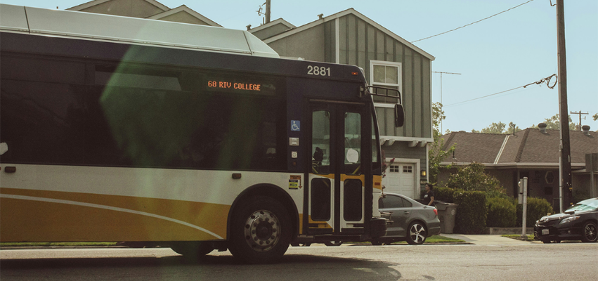Yellow and white city bus travelling along a residential street.