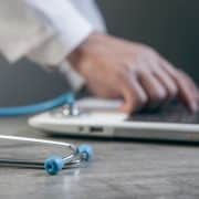Doctor using a laptop with a stethoscope on the desk, representing digital strategic planning in hospital systems.