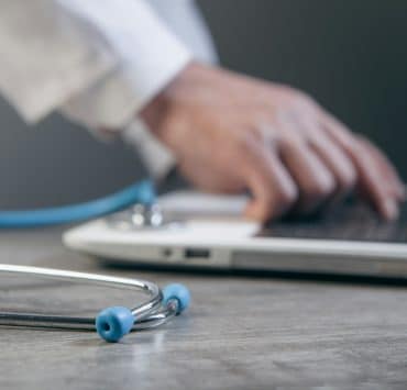 Doctor using a laptop with a stethoscope on the desk, representing digital strategic planning in hospital systems.