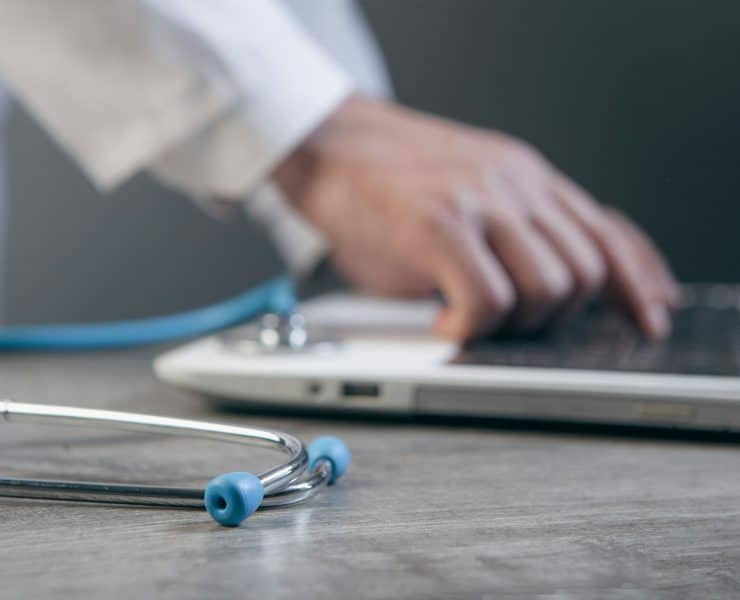 Doctor using a laptop with a stethoscope on the desk, representing digital strategic planning in hospital systems.
