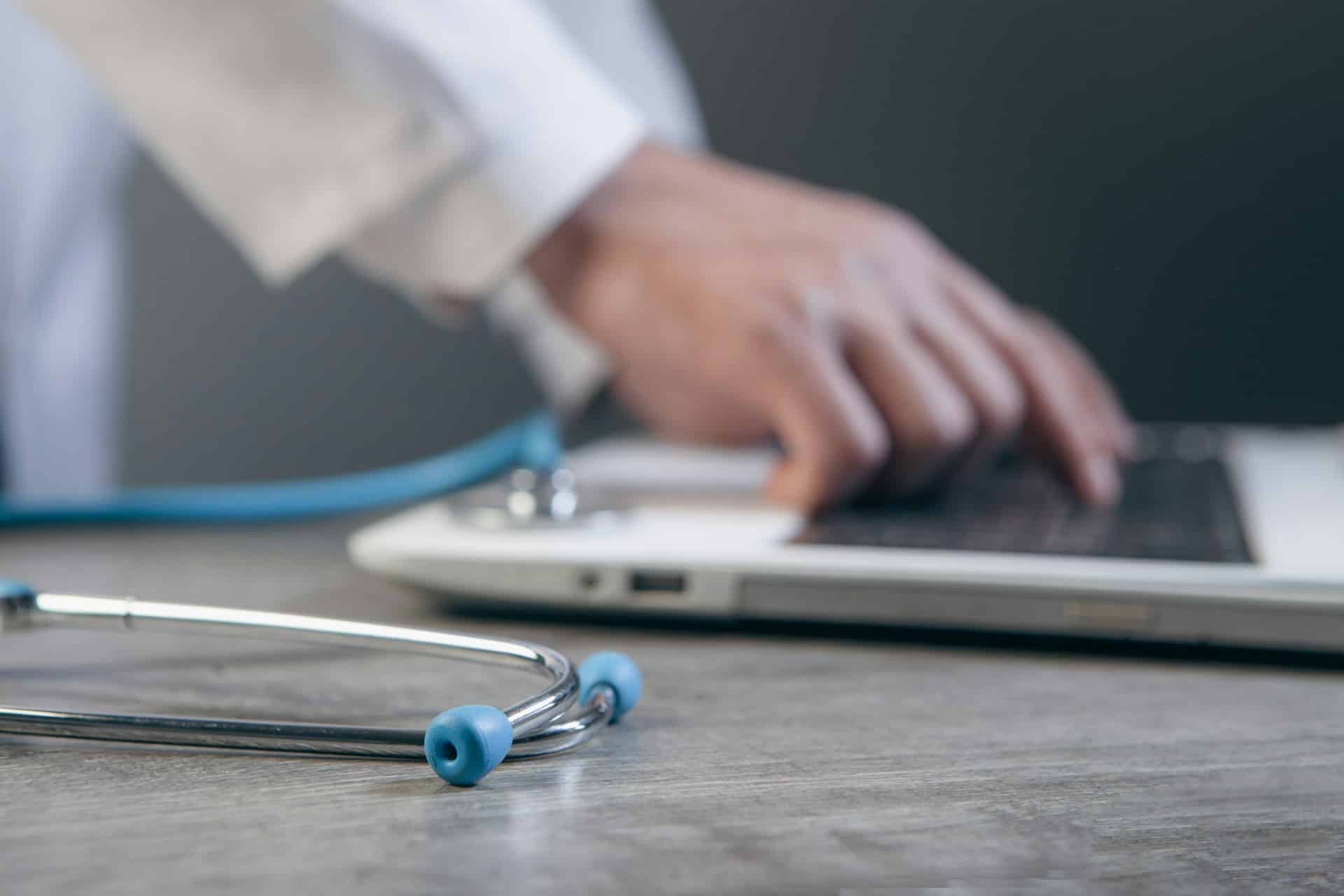 Doctor using a laptop with a stethoscope on the desk, representing digital strategic planning in hospital systems.