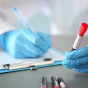 Gloved clinician holding a blood sample tube while writing notes on a clipboard